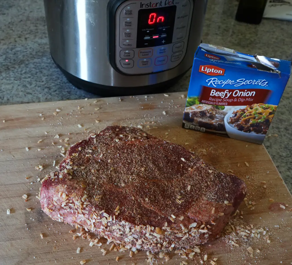 A raw roast seasoned with Lipton Beefy Onion recipe mix on a wooden cutting board, with an Instant Pot in the background.