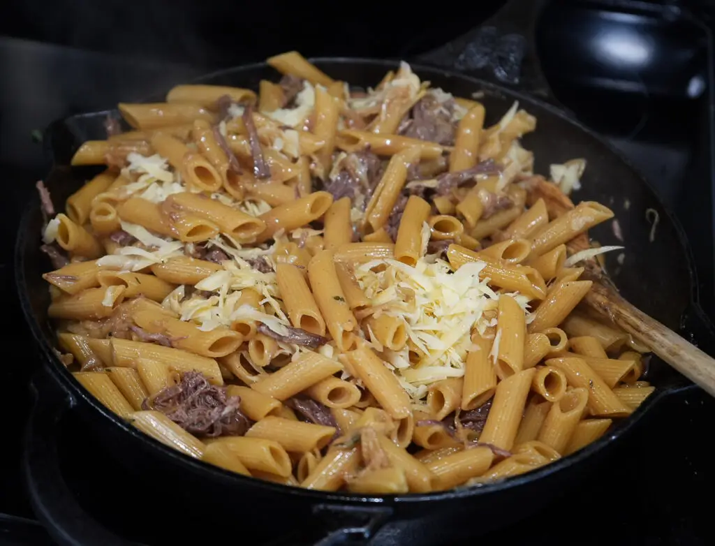 Penne pasta with shredded beef and melted cheese in a cast-iron skillet.