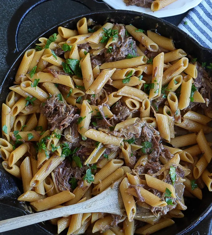Penne pasta with shredded beef in a cast-iron skillet, garnished with chopped parsley.