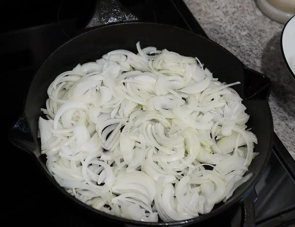 Sliced raw white onions filling a cast iron skillet.