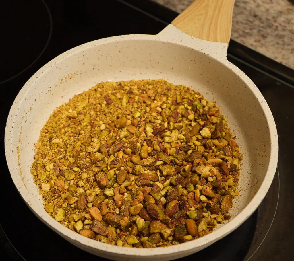 Chopped pistachios in a speckled white skillet on a stovetop.
