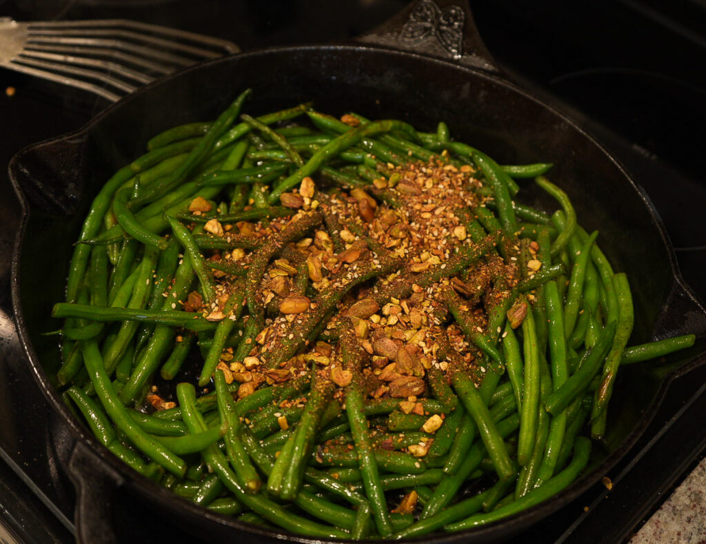 Cast iron skillet filled with green beans topped with chopped nuts and seasoning.
